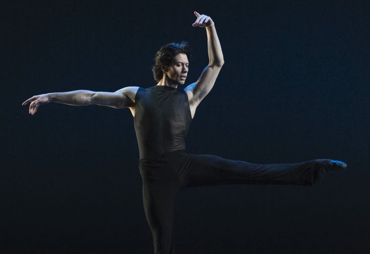 A ballet dancer balances on his right leg, his left leg outstretched at hip height. His right arm sticks straight out at shoulder height, and his left arm arcs over his head.